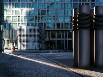 Moderne Gebäude und Skulpturen in urbanem Platz mit Gegenlicht.