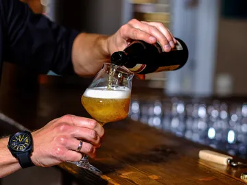 A glass of beer is poured from a bottle into a bar.
