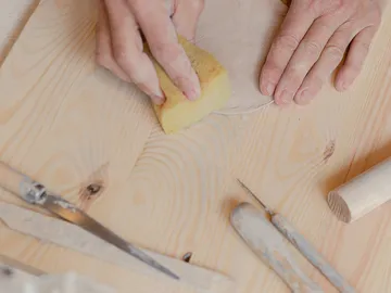 Hände bearbeiten Ton mit Schwamm auf Holzoberfläche.