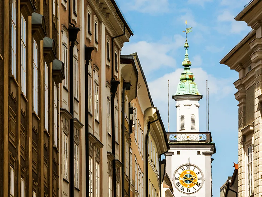 Uhrturm zwischen historischen Gebäuden unter blauem Himmel.