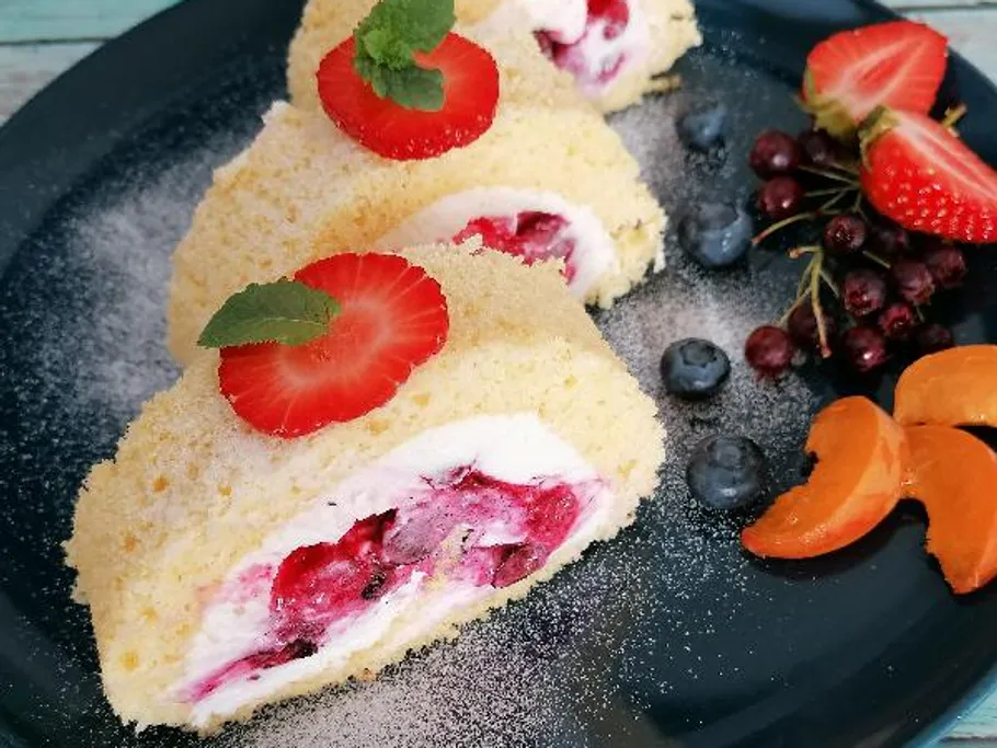 Gerollte Kuchenscheiben mit Beeren auf einem Teller.