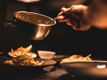 One hand lifts a sauce over a plate of food.
