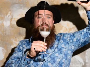 Bartender pours milk into a wine glass against background patterns.