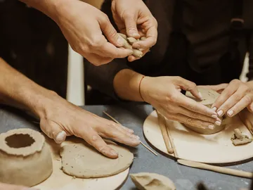 Hands form clay together in a creative workshop.
