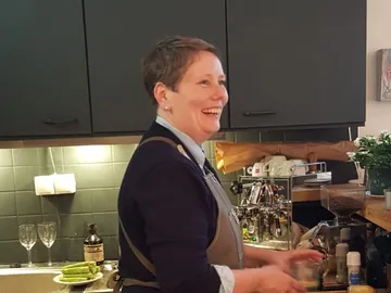 Woman smiles and mixes drinks in a modern kitchen.