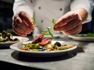 Cook garnished a dish with fresh herbs on the table.