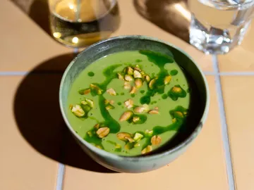 Green soup with nuts, in a bowl, on table.