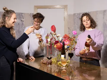 Three people toast, flowers and wines decorate the table.