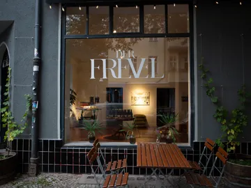 Window shows stylish café with plants and furniture.