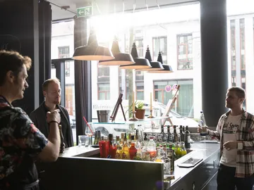 Drei Männer unterhalten sich an einer Bar mit Getränken.