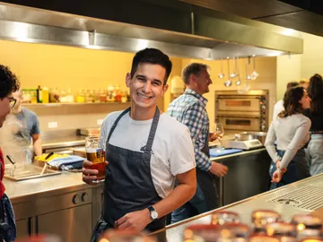 Junger Mann lächelt mit Bier in einer Restaurantküche.