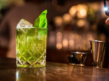 Grüner Cocktail mit Eis und Basilikum auf Bartresen.