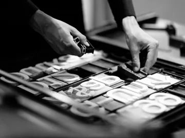 Hands arrange letters in a printing press.