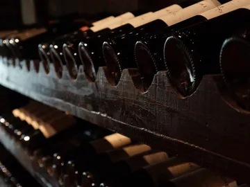 Wine bottles lie on a wooden rack in dim lighting.