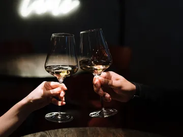 Two wine glasses toast in a dark restaurant.
