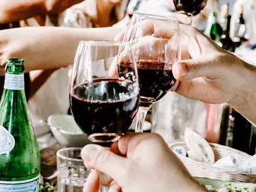 Glasses of red wine are held together to toast.