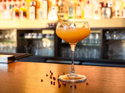 A cocktail is sitting on a wooden table surrounded by glasses.