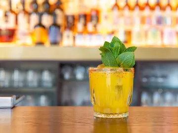 Glass with yellow drink, fresh mint, bar background.