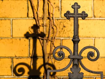 Black metal cross casts shadow on yellow brick wall.