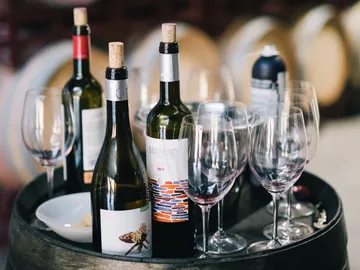 Bottles of wine are on a barrel, glasses are ready.