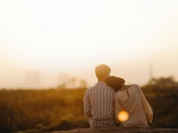 A couple sits close https://media.gokonfetti.com/28779/-/6503c8b03430e3205586396e0710e0df.webpbeieinander, hugging at sunset.