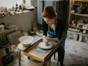 Eine Töpferin formt Ton auf einer Töpferscheibe in einem Atelier.