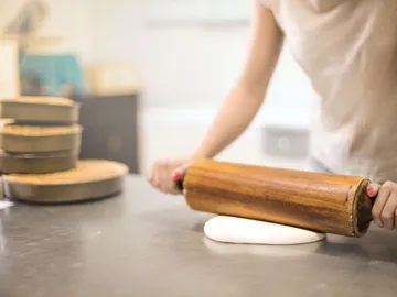 A person rolls dough on a table with a rolling pin.