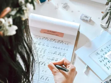 A person writes letters in a notebook on a table.