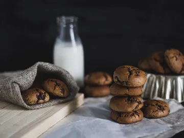 Cookies lie on a wooden board next to a milk bottle.