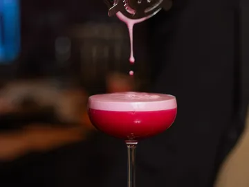 Ein Cocktail wird in ein Glas gegossen, Hintergrund unscharf.
