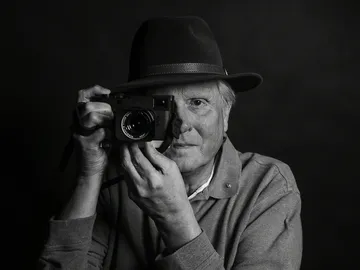 A man is holding a camera and looking straight into it.