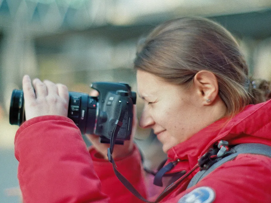 Frau fotografiert mit Kamera in roter Jacke draußen.