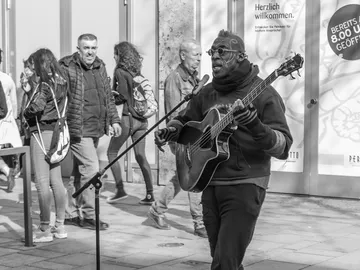 A musician sings and plays guitar in the street.