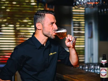 Mann trinkt Bier in einer Bar mit Gläsern im Hintergrund.