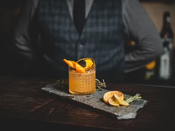 Ein Cocktail steht auf einem Steinbrett neben Zitrusfrüchten.