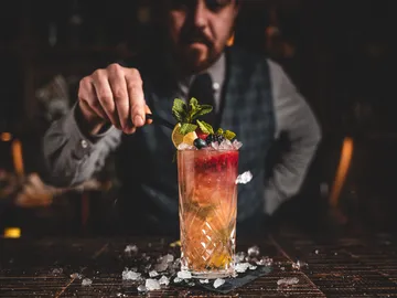 Bartender decorates glass with cocktail and fresh ingredients.