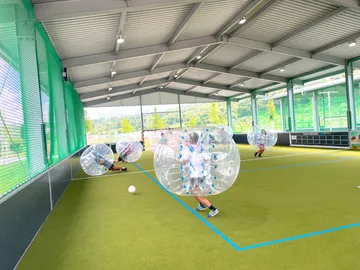 Players in air balls play soccer in a hall.