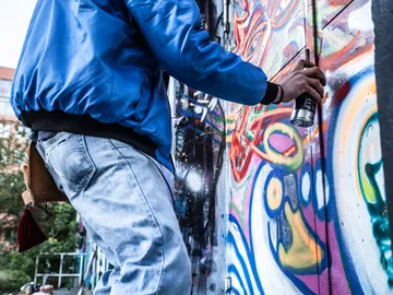 Junge sprüht Graffiti an bunte Wand im Freien.