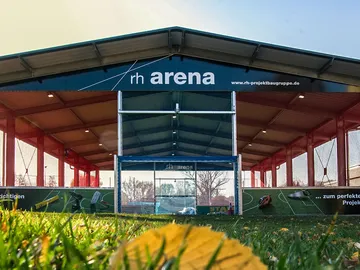 Sporthalle mit Netz, Fußballtor, grüner Rasen darunter.