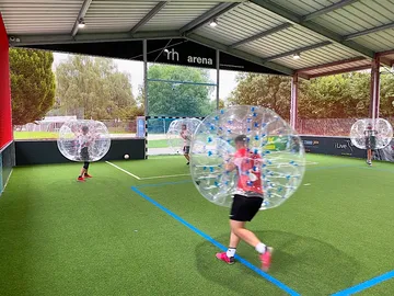 Transparente Bubbles, spielende Personen auf einem Kunstrasenfeld.