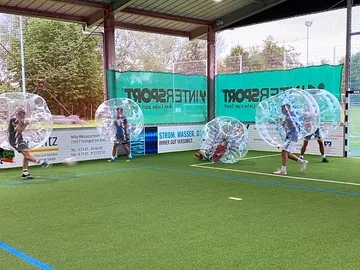 Spieler in durchsichtigen Bubbles laufen auf dem Fußballfeld.