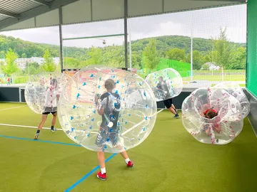 Kugelförmige Blasen umgeben spielende Kinder auf Rasenplatz.