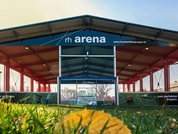 Sports arena with gate, surrounded by green grass and light.