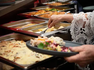 Eine Hand schöpft Essen von einem Buffet.