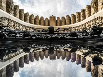 Reflektierende Oberfläche unter architektonischem Detail und Himmel.