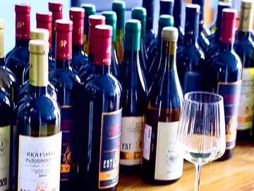 Wine bottles are close together, a glass is next to it.