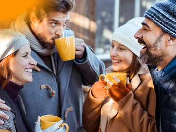 Vier Personen trinken Kaffee und lachen in der Sonne.