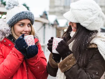 Zwei Frauen halten heiße Tassen in kalter, verschneiter Umgebung.