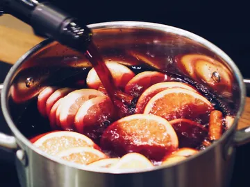 Topf mit Glühwein, Orangen- und Zimtstücken wird gefüllt.