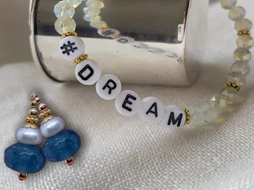 Bracelet with 'DREAM', earrings next to it, on a fabric background.